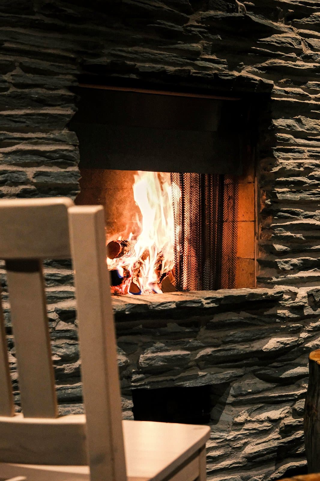 A dark slate stone fireplace with a real fire burning, warm close-up mood.
