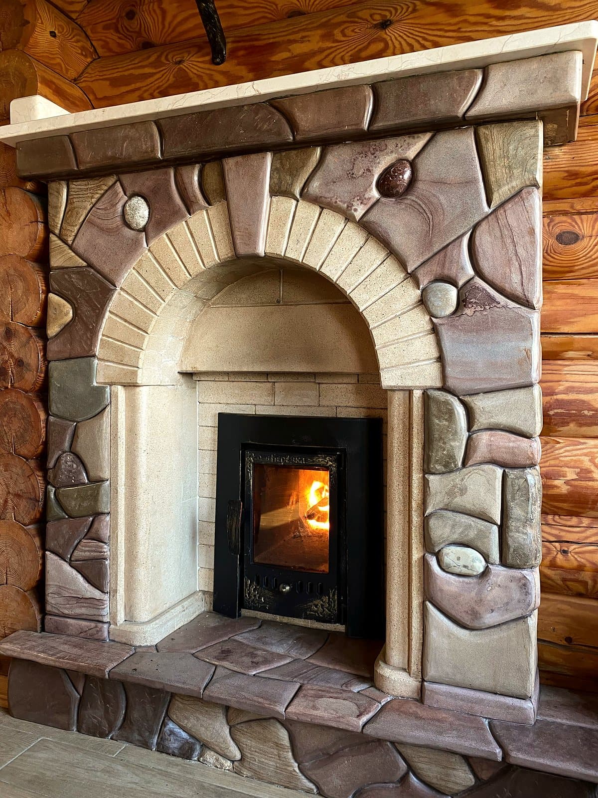 A custom carved stone fireplace with an arched opening, inlaid decorative stones, and hand-shaped keystones.
