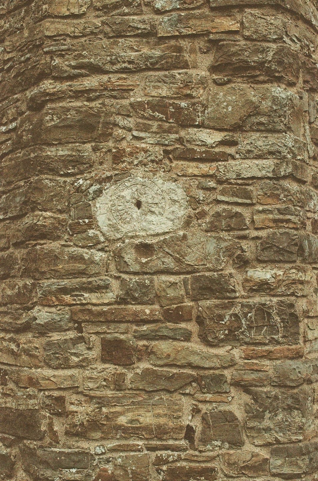 A circular carved stone medallion set into a weathered field-stone wall with horizontal coursing.