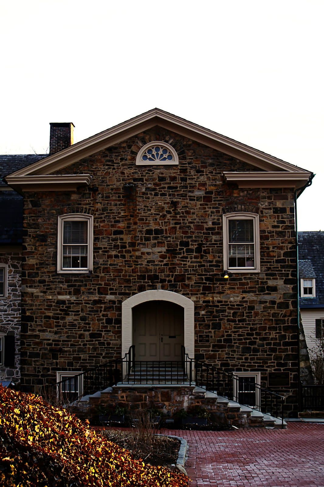 The stone facade of an old chapel with a pediment and a fanlight window over the entrance.